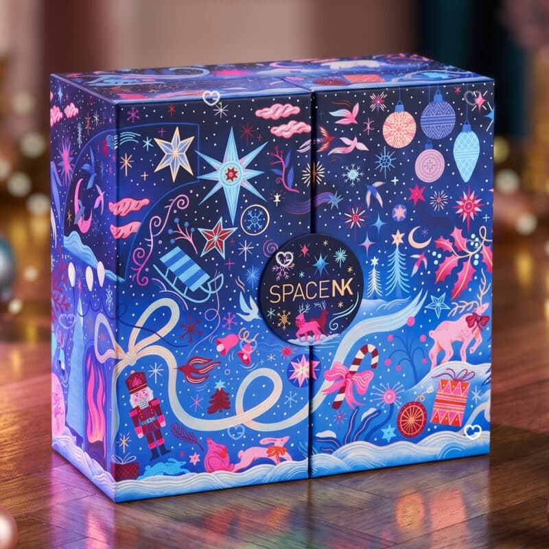 Calendrier de l'Avent beauté Space NK 2026 sur un parquet, lumières de Noël en fond