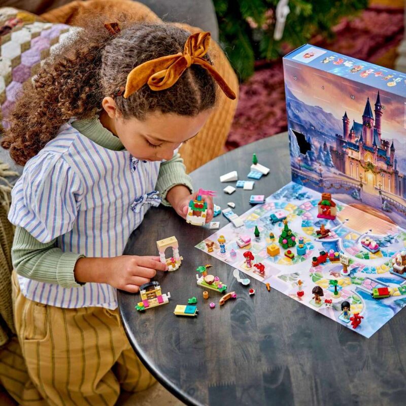 Enfant construisant le calendrier de l'Avent LEGO Disney 2026 sur une table, boîte et pièces déployées