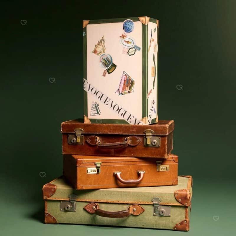 Calendrier de l'Avent Vogue 2026 posé sur des valises de voyage vintage empilées
